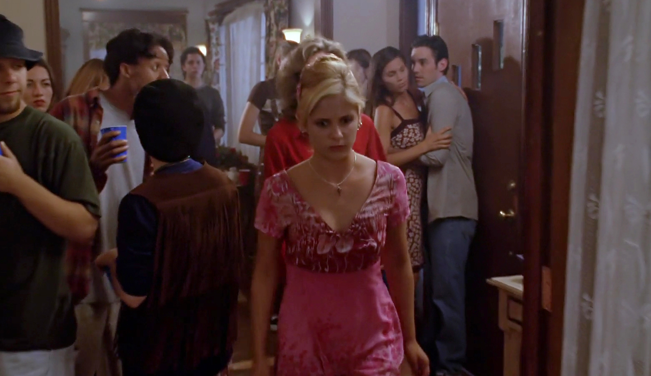 Buffy looks sad in the middle of a party in her house, as guests look over at her.